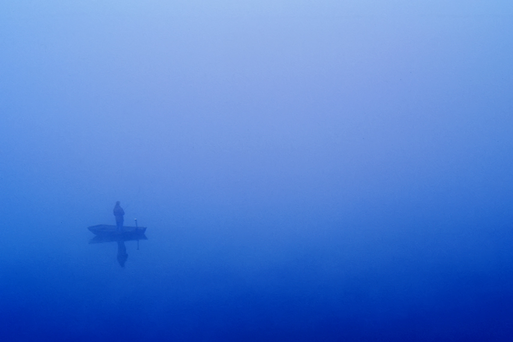 man fishing in boat in blue fog